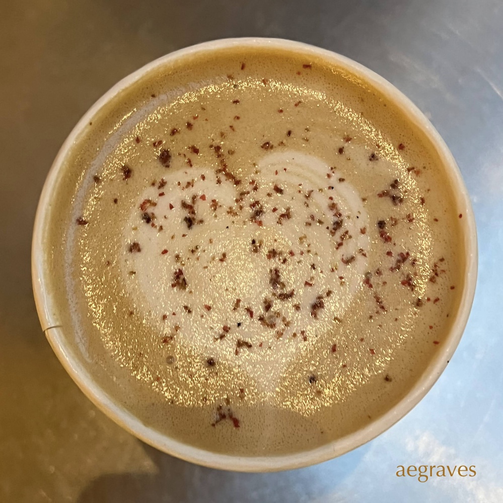 Image of an almond milk latte with ground pink peppercorns on top.