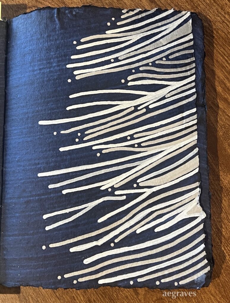 Right hand page of an indigo painted handmade paper journal with silver and white curved lines rising toward the right edge